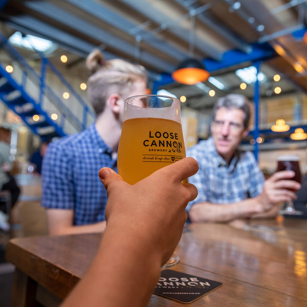 People sitting at a bar with drinks, focusing on a glass of 'Loose Cannon' beer.